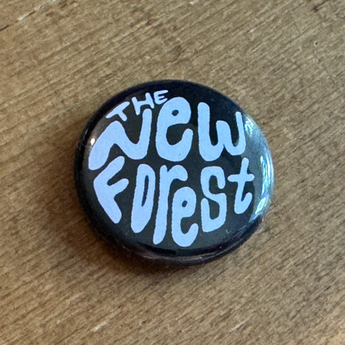 Black button badge with 'The New Forest' text on a wooden surface