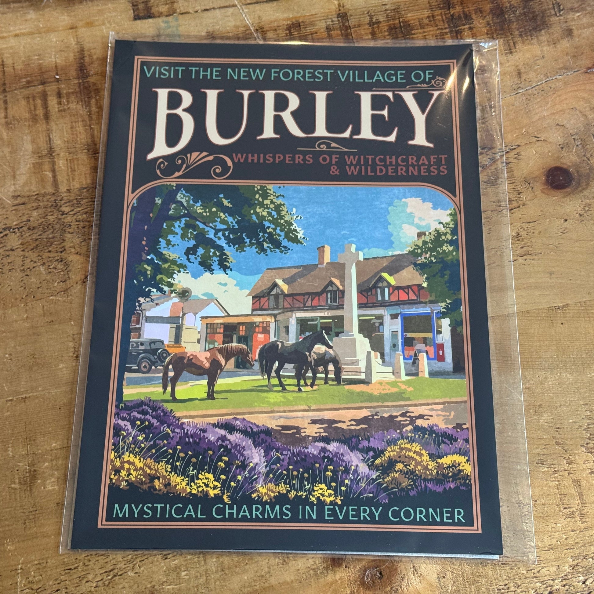 Promotional poster for the New Forest Village of Burley on a wooden surface, in protective film.